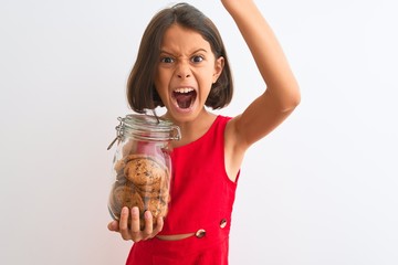 Beautiful child girl holding jar of cookies standing over isolated white background annoyed and frustrated shouting with anger, crazy and yelling with raised hand, anger concept