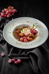 Grilled duck or turkey poultry fillet with berry sauce with baked grapes and caramelized onions. Restaurant menu. Background black boards.
