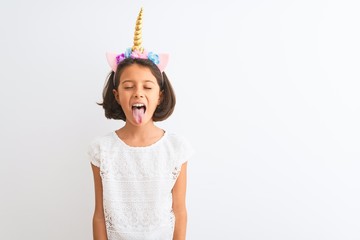 Beautiful child girl wearing unicorn diadem standing over isolated white background sticking tongue out happy with funny expression. Emotion concept. © Krakenimages.com