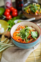 Bowl of stir fried udon noodles garnished with black sesame seeds and fresh mint with green chopsticks