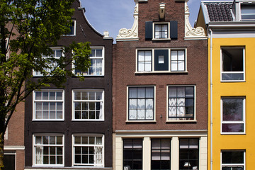 View of historical, traditional and typical buildings showing Dutch architectural style and a tree in Amsterdam. It is a sunny summer day.