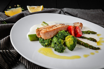 Diet nutritional fitness dish. Grilled turkey fillet with broccoli, asparagus, sweet pepper and sauce. Restaurant menu. Background black boards.