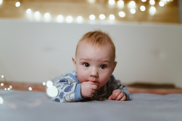little funny baby, very cute, lies on his stomach and holds a finger in his mouth