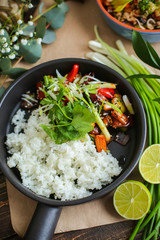 Bowl of stir fried udon noodles garnished with black sesame seeds and fresh mint with green chopsticks