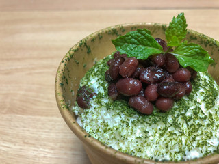 Green tea flavored shaved ice candy topped with red beans and mint leaves.