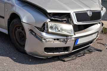 Obraz na płótnie Canvas Front of crashed silver car, deformed metal plates, hood, headlight and bumper