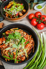 Bowl of stir fried udon noodles garnished with black sesame seeds and fresh mint with green chopsticks