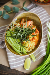 Bowl of stir fried udon noodles garnished with black sesame seeds and fresh mint with green chopsticks