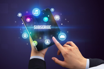 Businessman holding a foldable smartphone with SUBSCRIBE inscription, social media concept