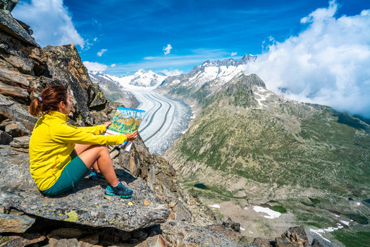Woman looking at map sitting on rocks at Eggishorn viewpoint above Aletsch Glacier, Bernese Alps, canton of Valais