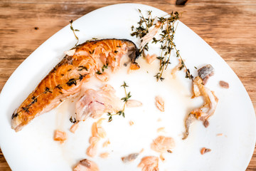Fried salmon fish steak , closeup. dirty dishes, a piece of red fish and bone on a plate. delicious dinner scraps.