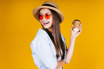 girl holds a paper cup with coffee in her hands and looks back over her shoulder, laughing happily. background yellow