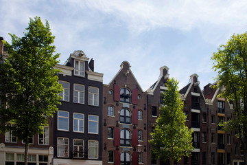 View of historical, traditional and typical buildings showing Dutch architectural style and trees in Amsterdam. It is a sunny summer day with blue sky.