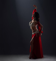 beautiful black-haired girl in red ethnic dress dancing oriental belly dance on stage in the dark