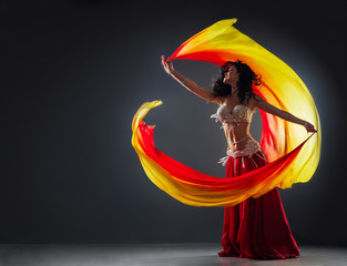 beautiful black-haired girl in red ethnic dress on the stage dances oriental dancing waving fabric...
