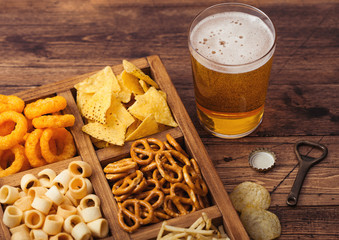 Glass of craft lager beer and opener with box of snacks on wooden background. Pretzel,salty potato...