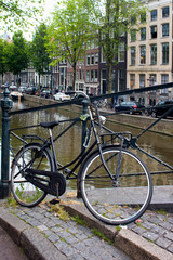 Fototapeta na wymiar Close up view of parked bicycle in Amsterdam. Canal, trees, cars and historical and traditional buildings are in the background. It is a summer day