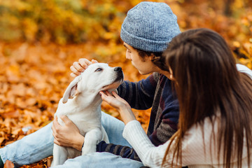 Romantic couple with dog sitting in autumn forest background with small dog. Young blonde woman and handsome man. Concept - family, togetherness, love, friendship.