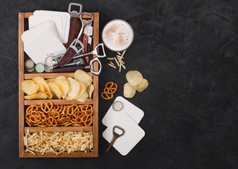 Glass of craft lager beer and opener with box of snacks on black background. Pretzel and crisps and...