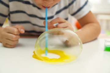 Little boy blowing slime bubble on white table, closeup