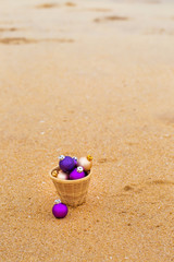 Fototapeta na wymiar Christmas balls in a basket on the sandy shore, top view