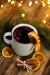 Obraz na płótnie Canvas Christmas hot mulled red wine in white mug with spices and fruits on a wooden rustic table. Traditional warming winter drink for holiday time. Cozy home atmosphere