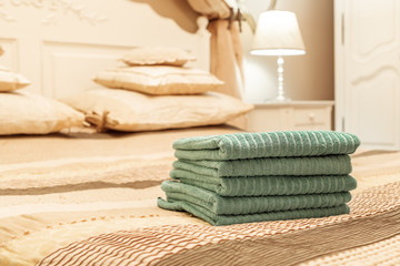 Stack of green hotel towel on bed in bedroom interior
