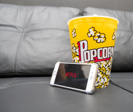 Ribeirao Preto, BRA - December 08, 2019: Sofa with popcorn bottle and Netflix logo on Apple phone . Netflix is a global provider of streaming movies and TV series.
