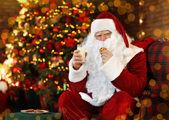 Santa Claus with milk and cookie near Christmas tree indoors