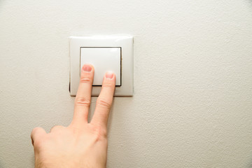 The hand presses the light switch. The concept of saving electricity, turning on the light in dark days.
