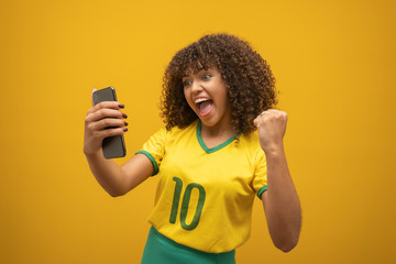 Supporter of the Brazilian football team celebrating a goal by watching the smartphone