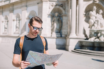 Man tourist with a city map and backpack in Europe street. Caucasian boy looking with map of European city.