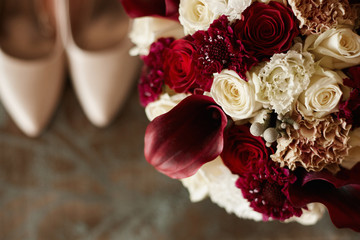Beautiful colorful wedding bouquet and bridal shoes out of focus. Fashionable bridal bouquet of peonies, roses, and exotic flowers. Closeup shot of wedding fashion. Background for wedding invitation