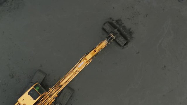 Top down aerial view of a digger moving mud on a construction site.