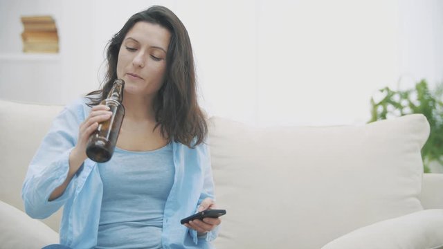 Slowmo. Tipsy brunette woman is chatting via smartphone, holding a bottle of beer and drinking it.
