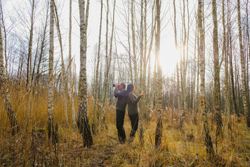 Happy couple with binoculars on a walk in the birch forest. Back to back couple in the morning sun.