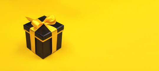 One black gift box on yellow background. Holiday concept.