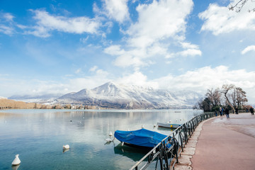 Cute European landscape of the lake. Photo of the pier and blue clear water on the background of snow-capped mountains. Quiet pier with boats on the shore of a mountain lake