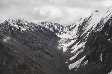 Atmospheric minimalist alpine landscape of big snowy mountain with massive glacier. Cloudy sky over great rocky mountains. Glacier tongue near snowbound mountainside. Majestic scenery on high altitude