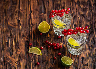 Gin Tonic with red currants, ice and lime, on a wooden background. View from above.