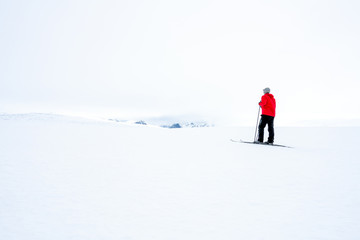 Man in red jacket doing cross country skiing during foggy weather in the mountains of Norway,...