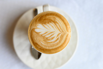 Cup of cappuccino with a beautiful pattern on the foam on the white plate and the table