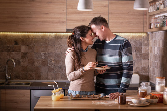 Married Couple Eating Cakes At The Kitchen.They Embrace Each Other And Kiss.