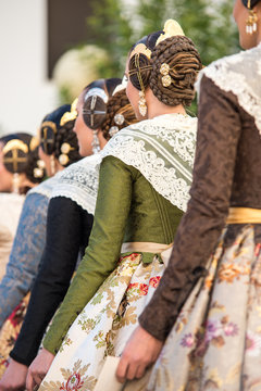Falleras seen from behind. Dresses with floral designs and typical hairstyle of the fallas with their jewels.
