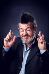 A portrait of bearded man with iroquois wearing suit covering showing crossed fingers. People and emotions concept