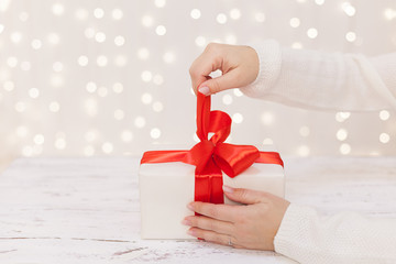 woman hands holding white box with red ribbon 