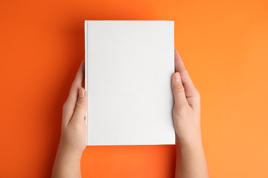 Woman holding book with blank cover on orange background, top view