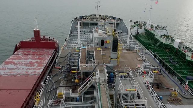 two vessels at Danish port roadstead moored to huge oil tanker for bunkering against sun reflection on ocean surface
