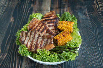 Grilled steak in a round bowl with spices, herbs and vegetables on a dark wooden background. Space for text.