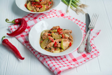 Hot salad with chicken, zucchini and chili pepper, sprinkled with sesame seeds and herbs. Asian food. Light wooden background.